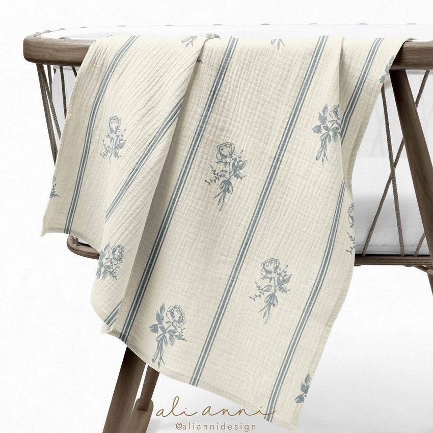 Crinkle muslin swaddle blanket mockup draped over a wooden crib with a white background, featuring blue floral and stripe patterns.
