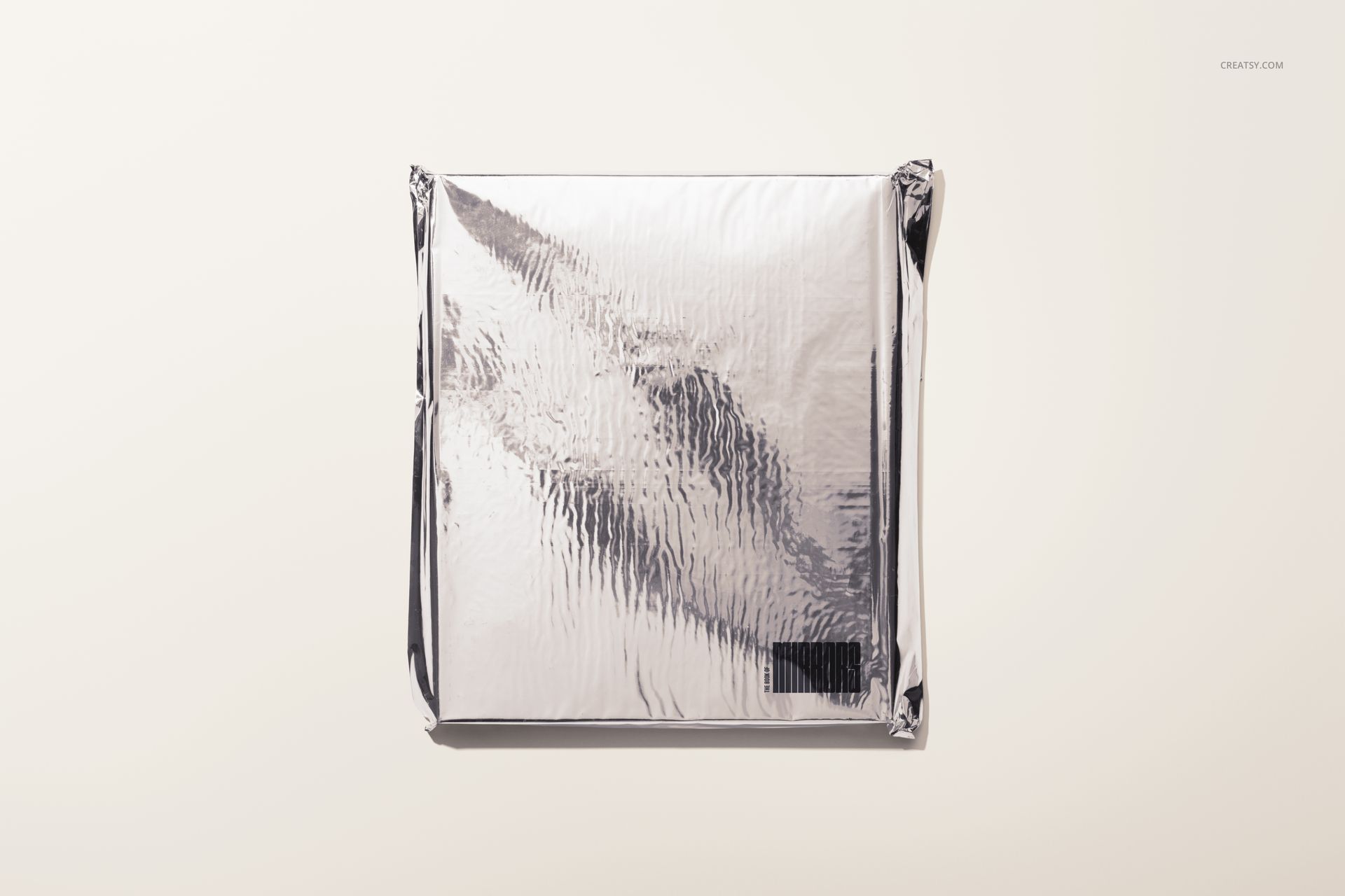 Hardcover book mockup with a silver, crinkled foil cover, shown from a top view against a light background.