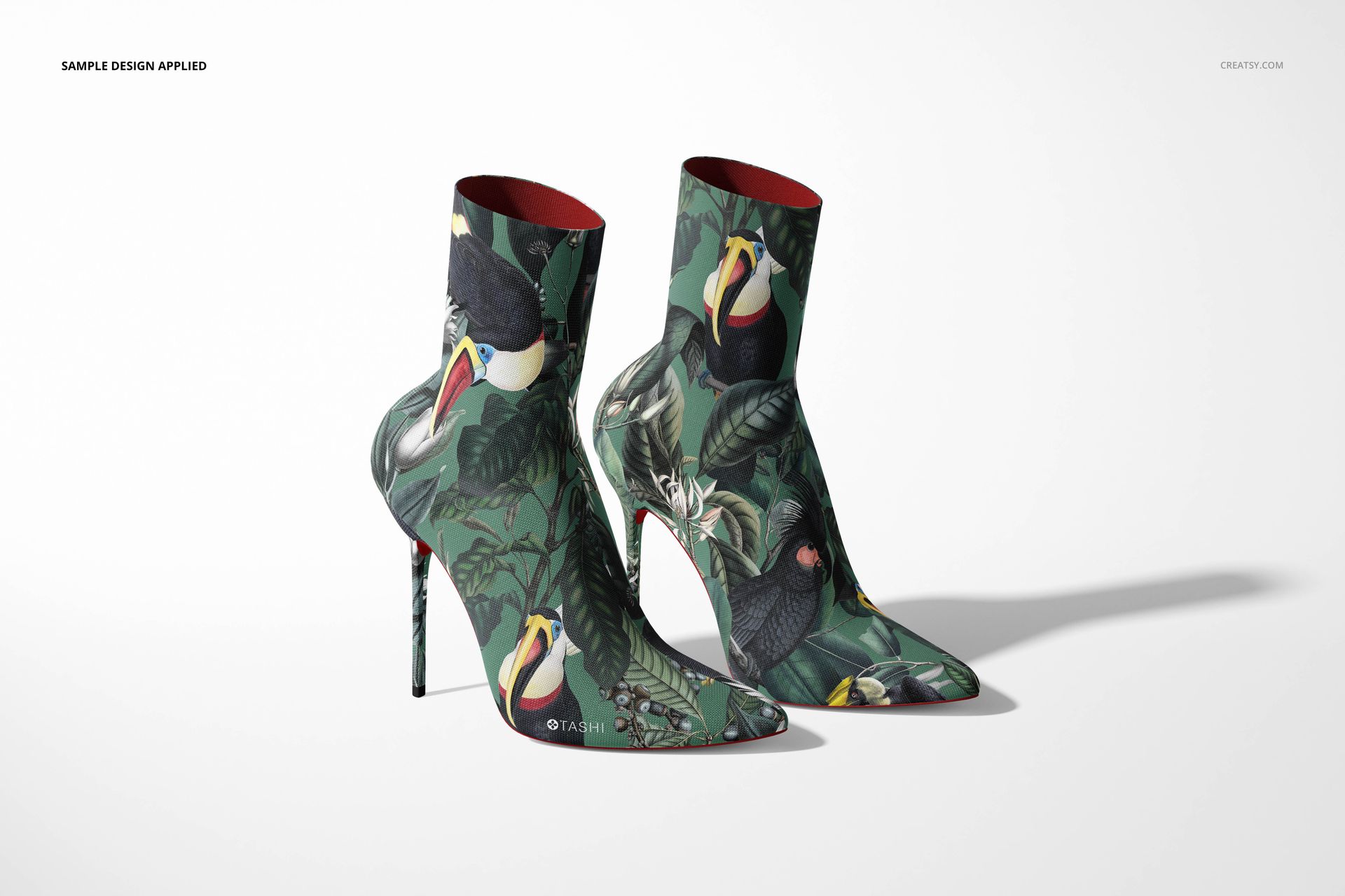 Two ankle boots featuring a green jungle motif with birds, displayed side by side in a realistic mockup scene.