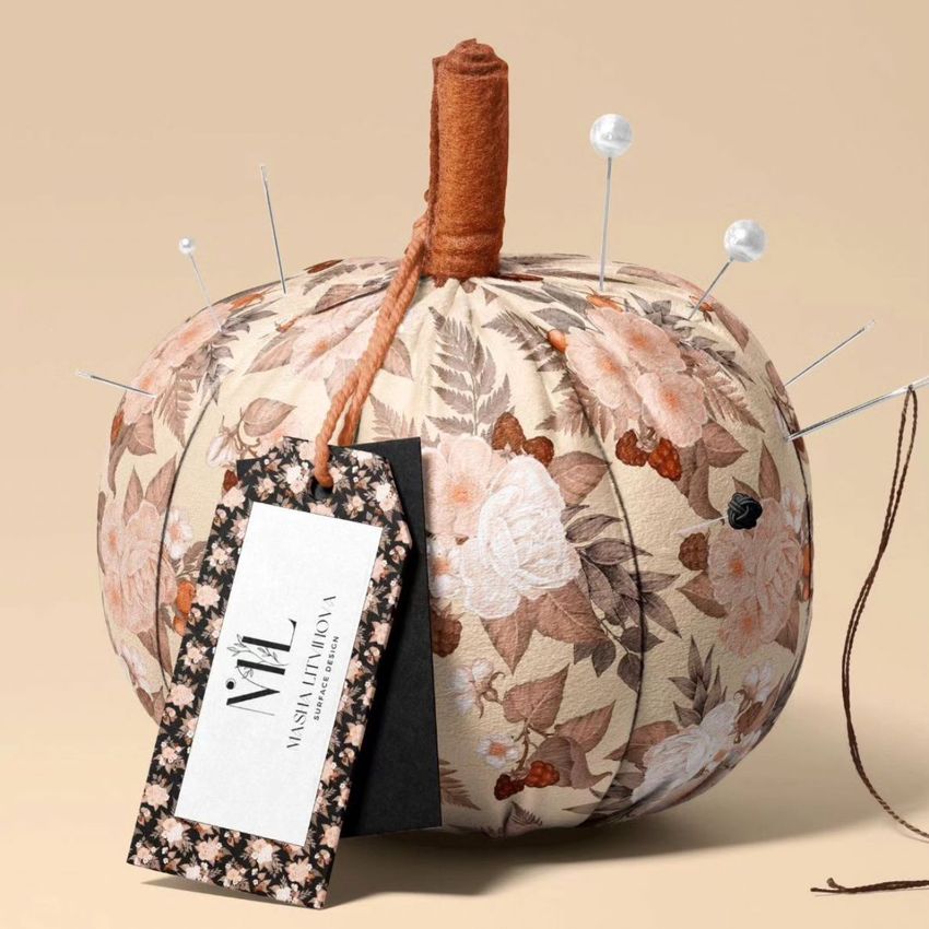 Fabric pumpkin mockup with a floral pattern in beige and brown tones, decorated with sewing pins and a tag attached to the stem.