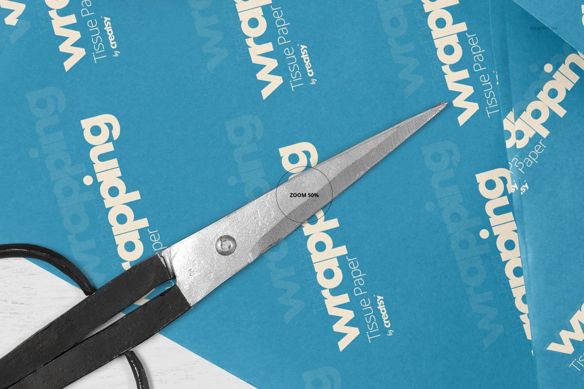 Blue wrapping tissue paper mockup with white text, shown in a close-up view with scissors placed on top.
