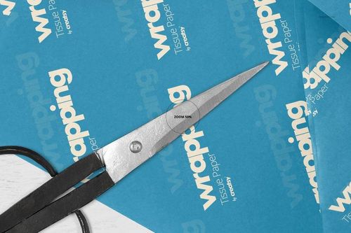 Blue wrapping tissue paper mockup with white text, shown in a close-up view with scissors placed on top.
