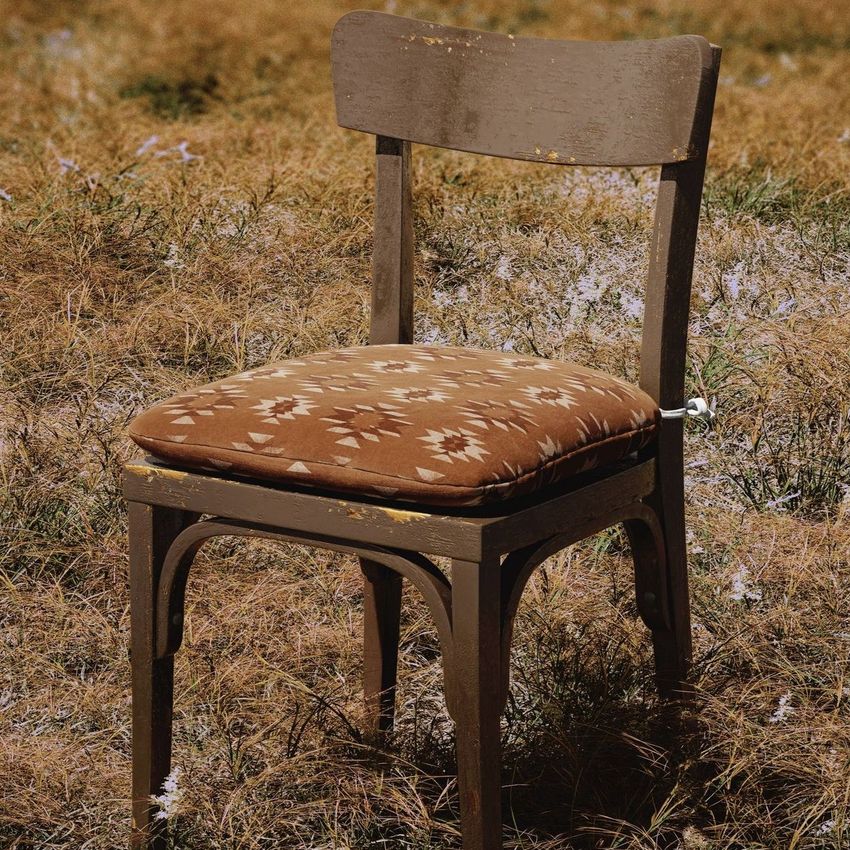 Rustic chair cushion mockup featuring a brown wooden chair with a patterned cushion, set outdoors on dry grass.