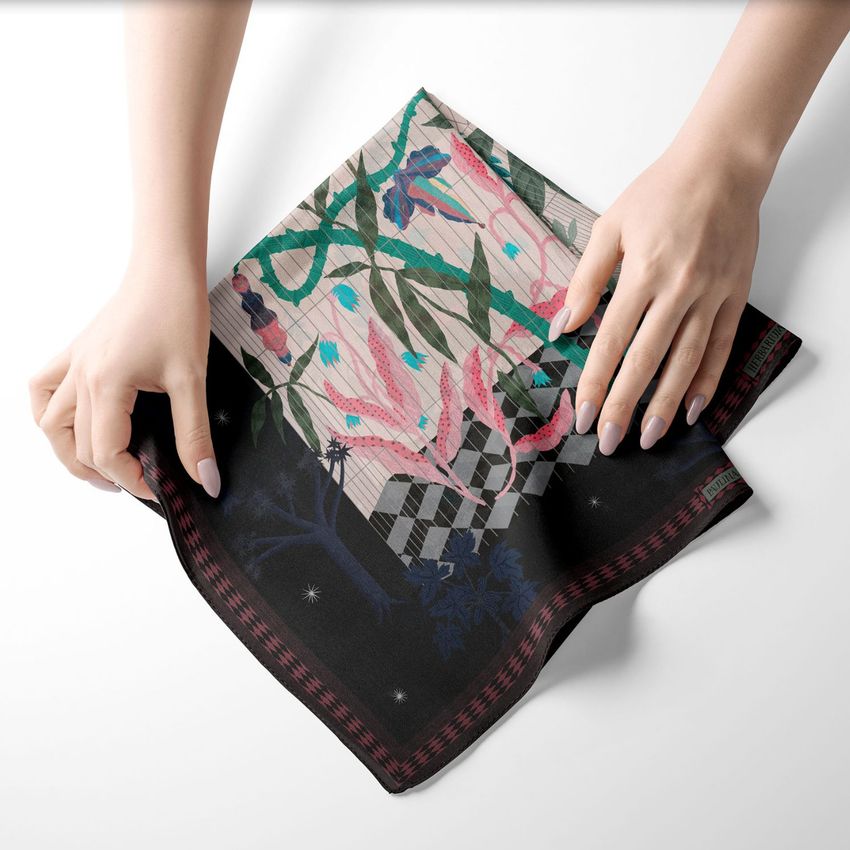 Hands gently hold a square silk scarf mockup featuring a botanical and geometric pattern in pink, green, and black on a white surface.