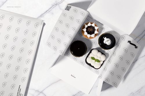 Top view of dessert packaging mockup with food safe paper, featuring assorted pastries in a white box on marble surface.