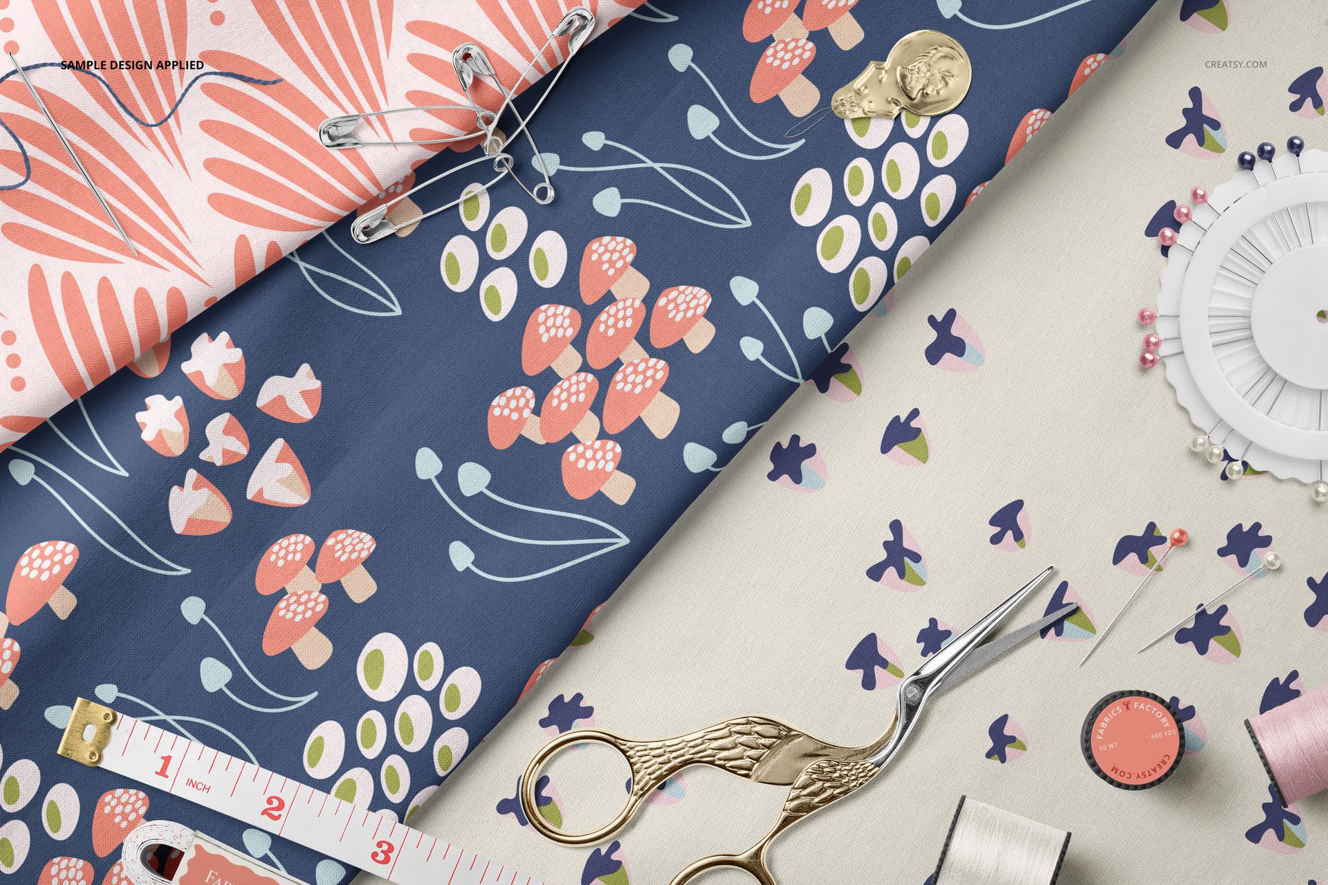 Top view of cotton fabric mockup featuring colorful designs and various sewing tools like safety pins, spool, and thimble.