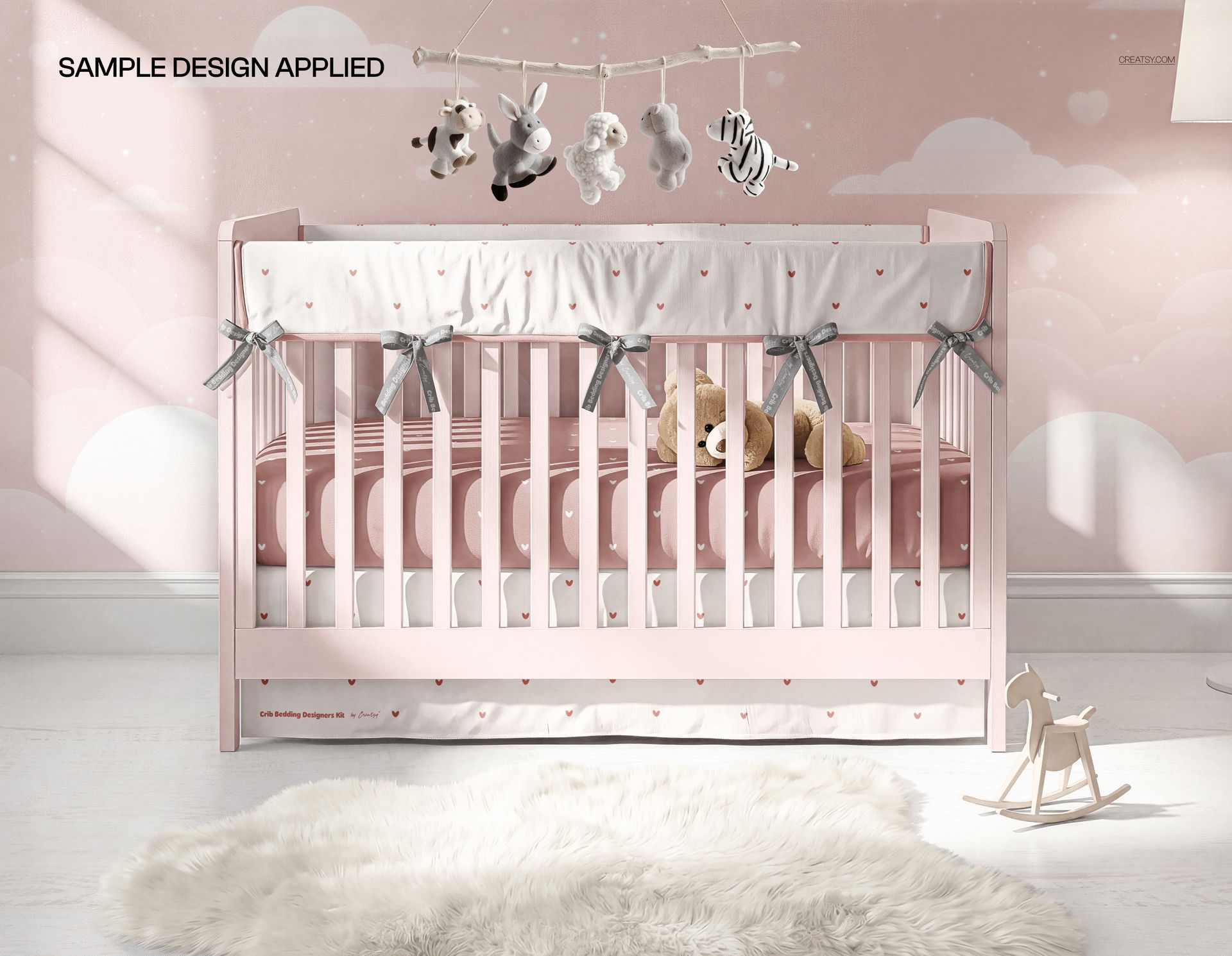 Nursery scene mockup featuring a crib with a decorative skirt and rail cover, soft pink background, and hanging mobile.