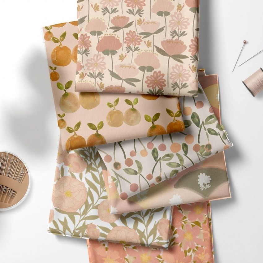 Folded fabrics mockup featuring six pieces of fabric with spring-themed floral and fruit patterns in pastel colors on a white surface.