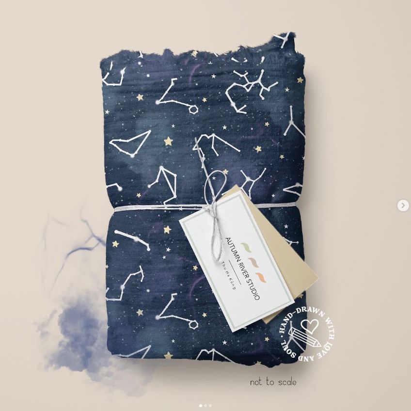 Muslin swaddle blanket mockup featuring a dark blue fabric with white constellation patterns, folded and tied with string and tags.
