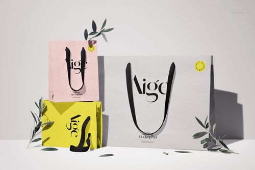 PSD mockup showing three paper gift bags in different colors, black ribbon handles, and olive branch accents on a light background.