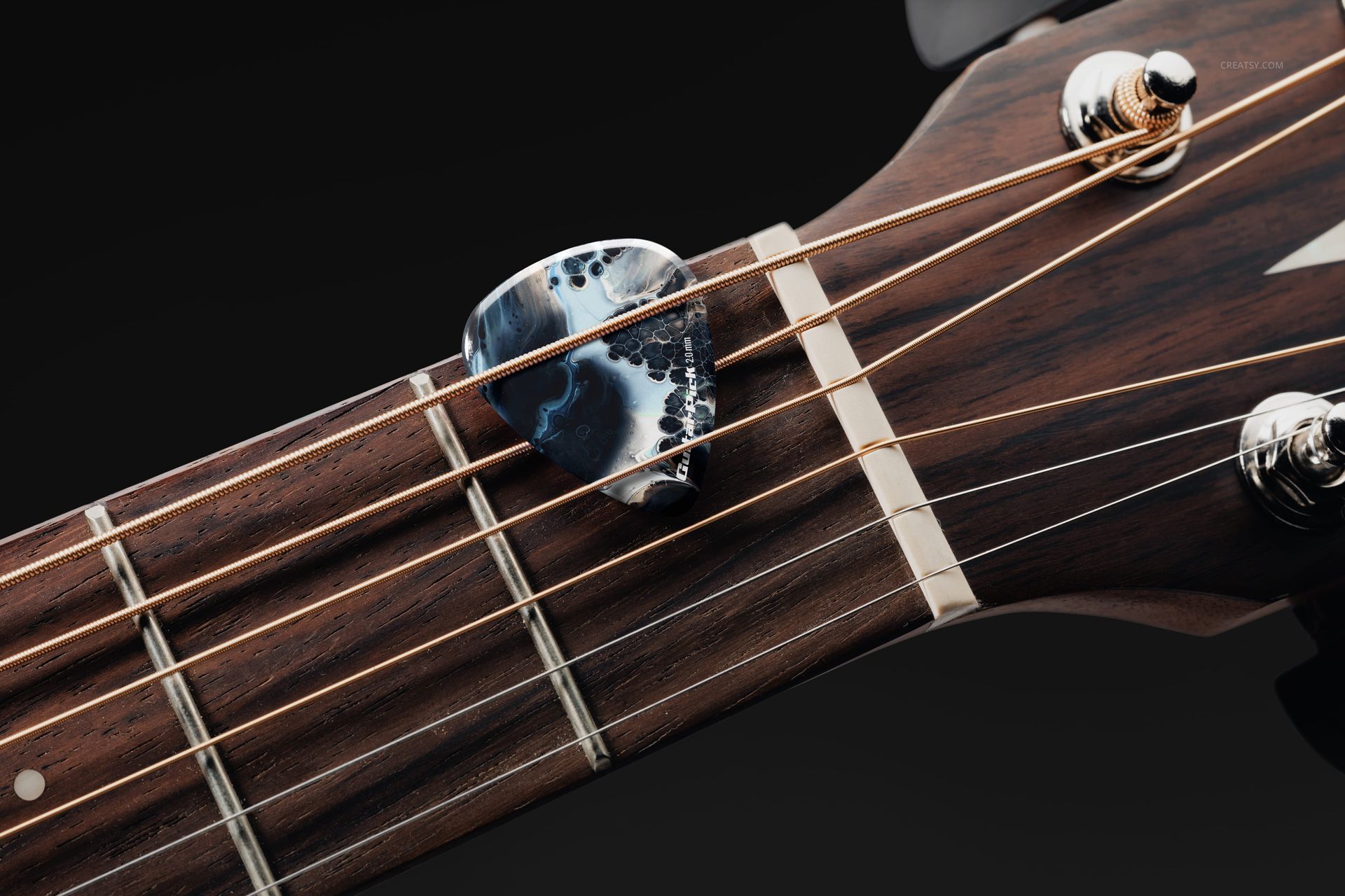 PSD mockup featuring a guitar pick with abstract blue and black design positioned across the strings of a classic guitar.
