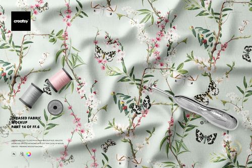 Top view of a light-colored fabric mockup featuring creases, floral branches, butterflies, and sewing tools nearby.