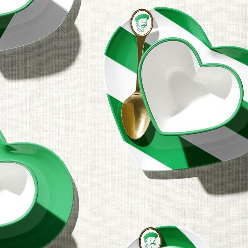 Heart-shaped cup mockup with a green and white striped saucer and gold spoon, viewed from above on a light fabric surface.