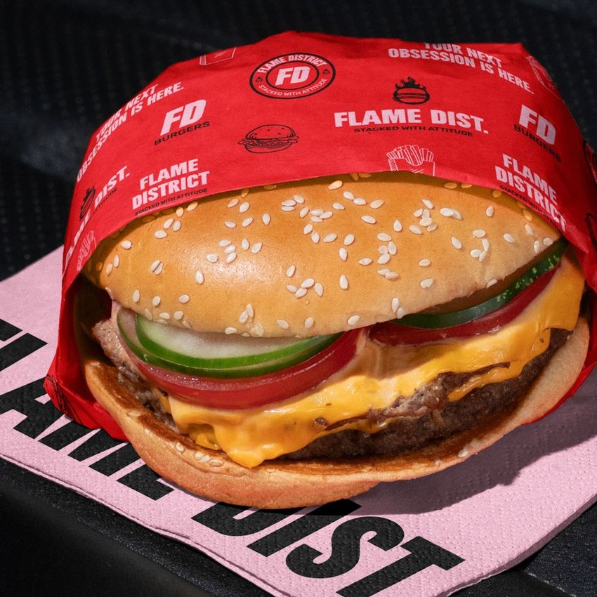 Burger mockup featuring a cheeseburger with lettuce, tomato, and pickles in branded red wrapping, placed on a pink napkin inside a car.