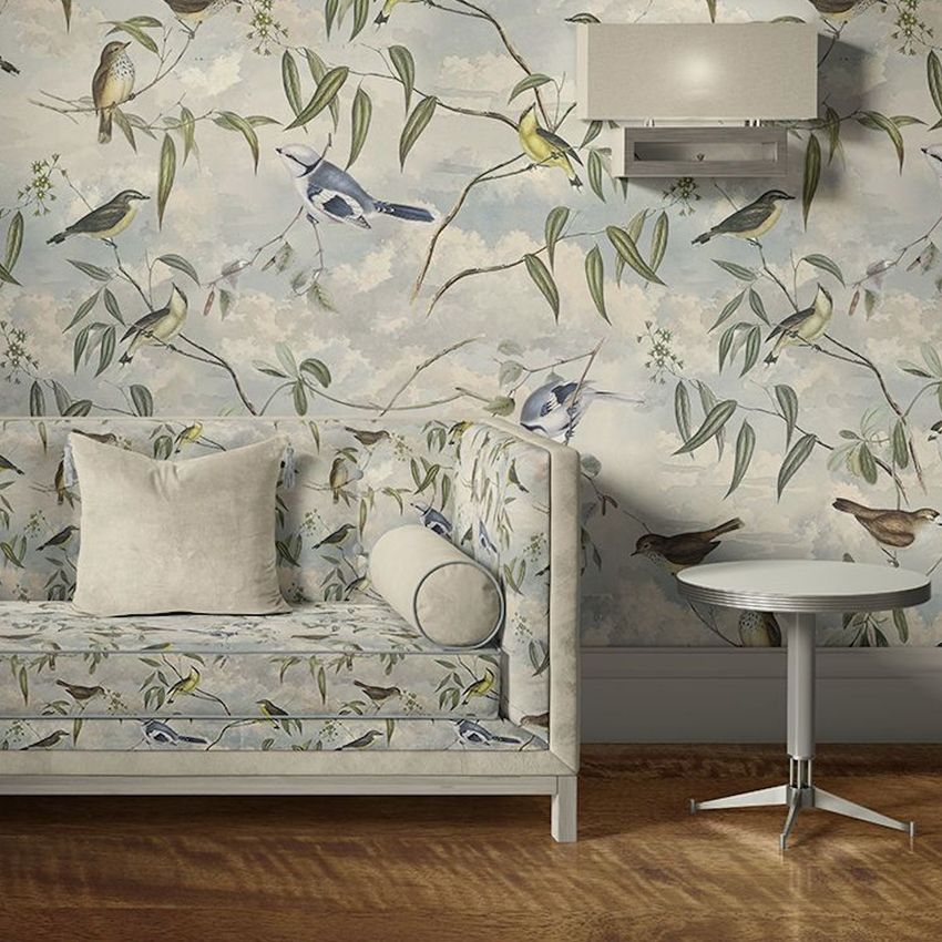 Velvet sofa and round coffee table mockup in a living room with bird and branch patterned wallpaper and wooden floor.