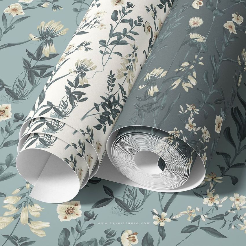 Paper wallpaper mockup featuring two rolled sheets with botanical floral patterns in muted blue and cream tones on a flat surface.
