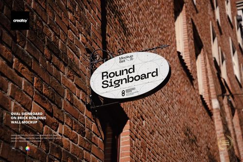 Oval signboard mockup mounted on a red brick building wall, shown from a side angle with sunlight and shadows.