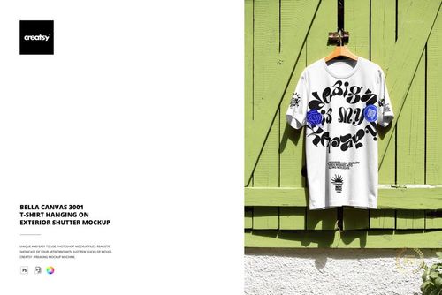 PSD mockup featuring a white short sleeve t-shirt with graphic elements, hung on a rustic green shutter outdoors.