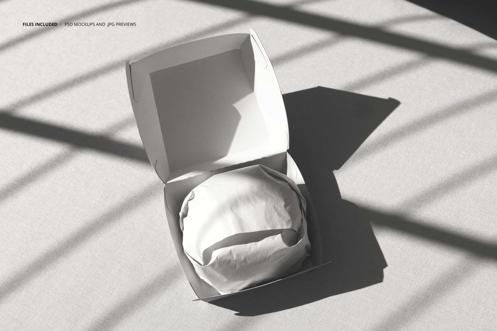 PSD mockup of an open burger packaging box with a wrapped burger, viewed from above on a light fabric surface.