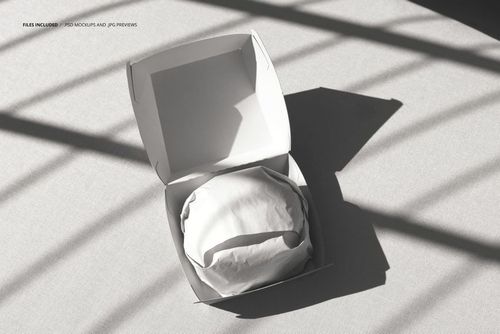 PSD mockup of an open burger packaging box with a wrapped burger, viewed from above on a light fabric surface.