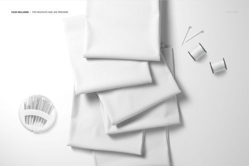 Stack of folded white fabrics arranged on a flat surface, viewed from above with sewing pins and spools nearby.