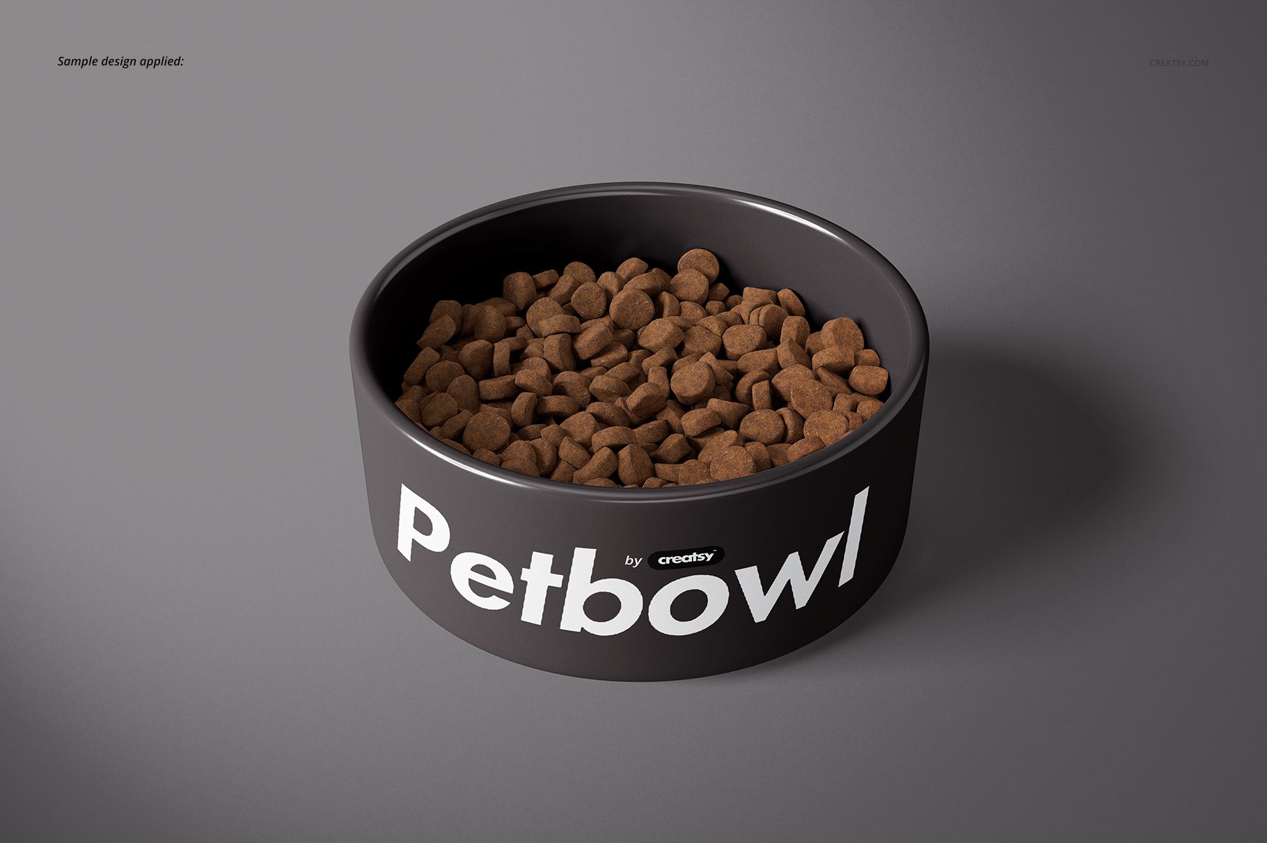Round pet bowl mockup with large white lettering, filled with dry pet food, displayed on a smooth gray surface.