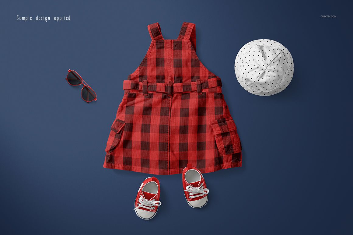 Front view of a baby dress mockup set featuring a red plaid dress, white polka dot hat, red sunglasses, and matching shoes on a blue background.