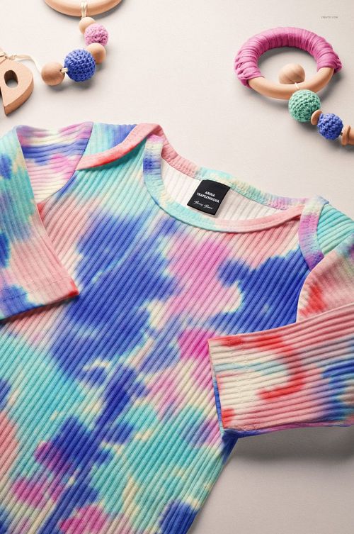 PSD mockup of a baby ribbed knotted gown in multicolor pastel tones, laid out next to wooden and crochet baby toys.