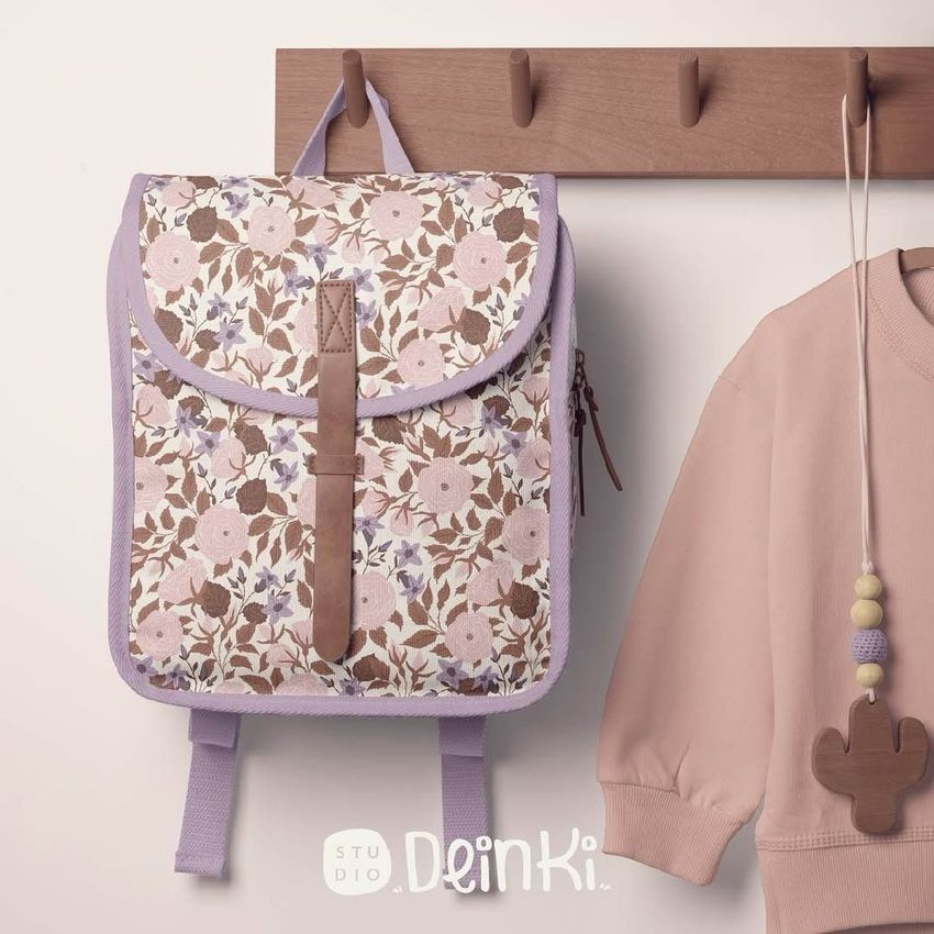 Kids backpack mockup with a delicate floral pattern in pastel pink and lavender, hanging on a wooden rack next to a soft pink sweatshirt.