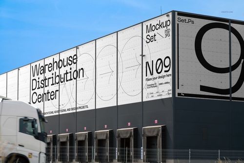 Large warehouse distribution center building with white and black exterior, featuring prominent mockup signage and truck in foreground.