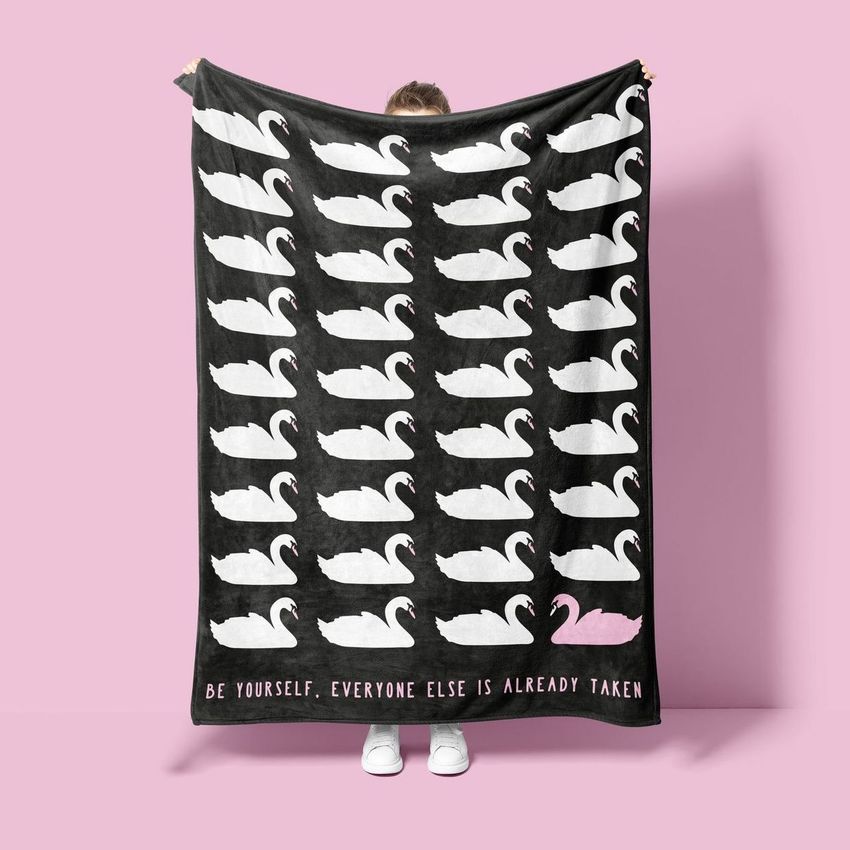 Person holding a fleece throw blanket mockup with white swan silhouettes and one pink swan, against a pink background.