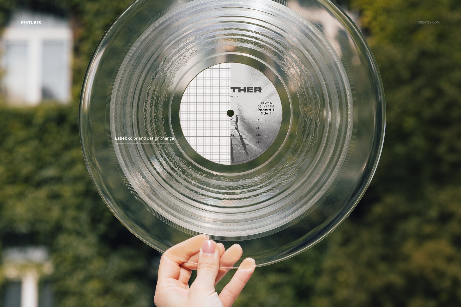 Close-up of a transparent vinyl record mockup held up outdoors, with green ivy and building windows in the background.