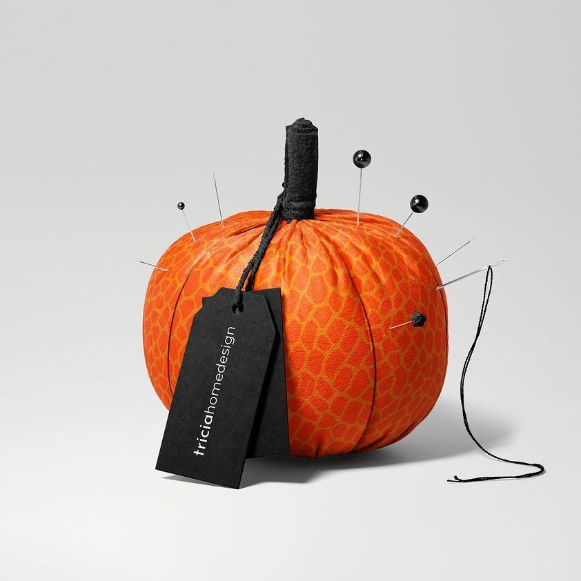Fabric pumpkin mockup featuring an orange patterned pumpkin with sewing pins, a black tag, and a black string on a light background.