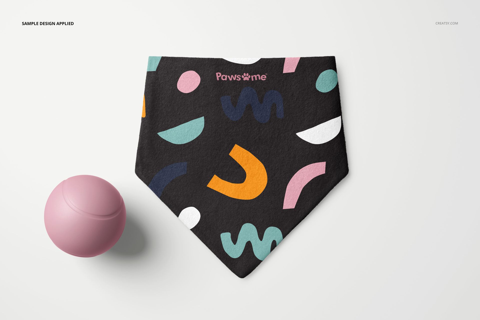 Dog scrunchie bandana mockup featuring a black fabric with multicolor geometric pattern, displayed flat with toy ball.