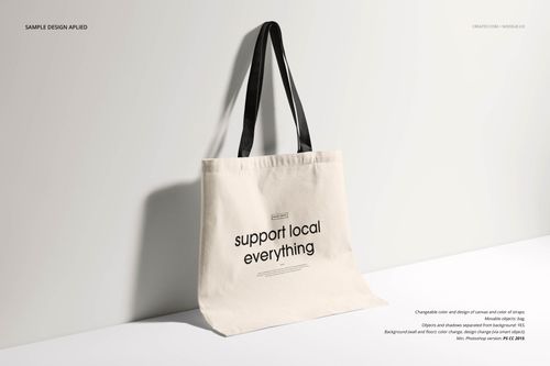 Beige fabric tote bag mockup with black straps, shown upright on a neutral surface with shadow detail.