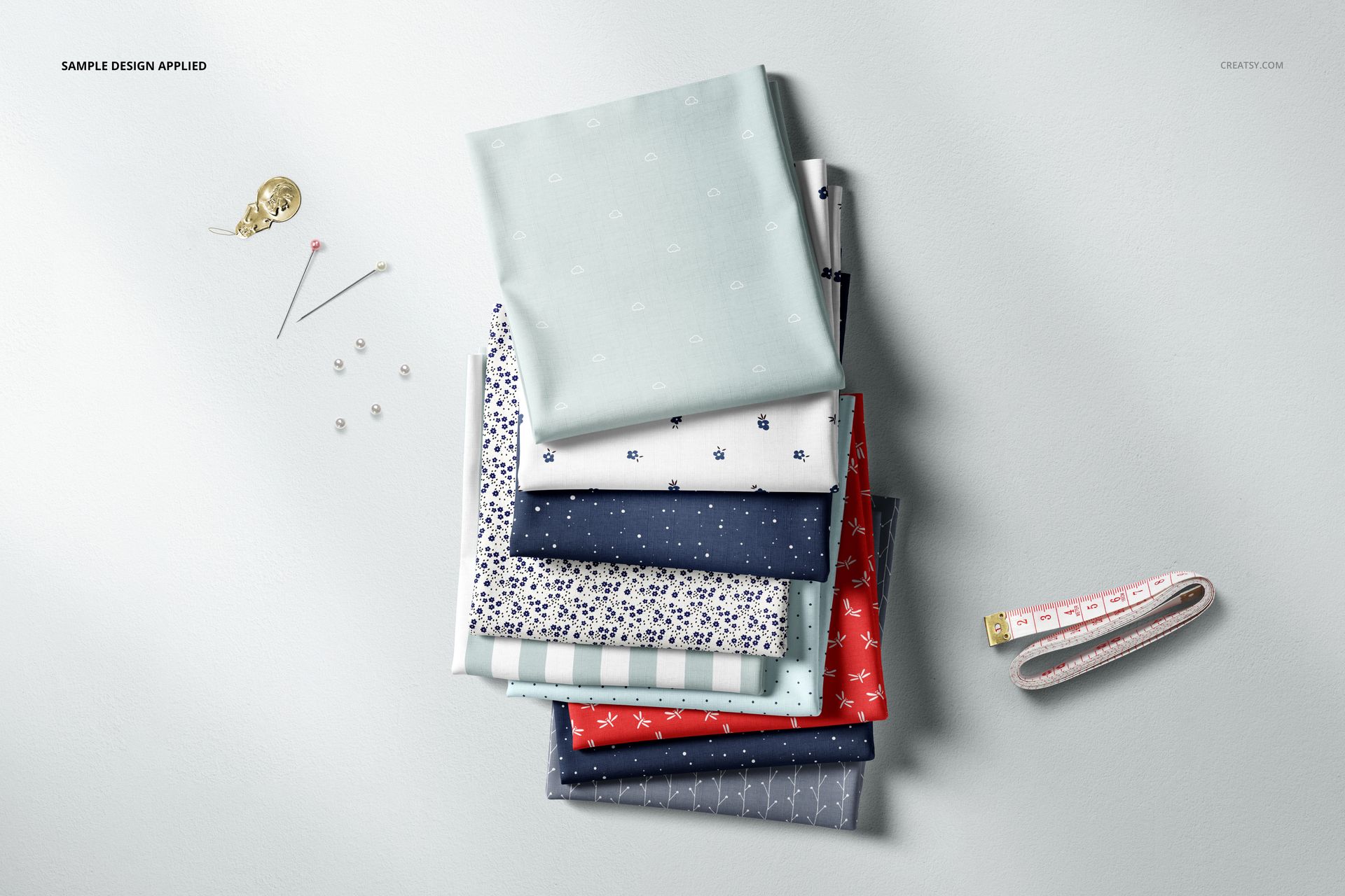Assorted fabric stack mockup featuring light blue, navy, and patterned textiles, viewed from above with pins and tape measure.