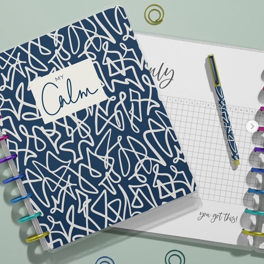 Overhead shot of spiral notebook mockup with colorful rings, abstract cover design, and an open planner with visible handwriting.