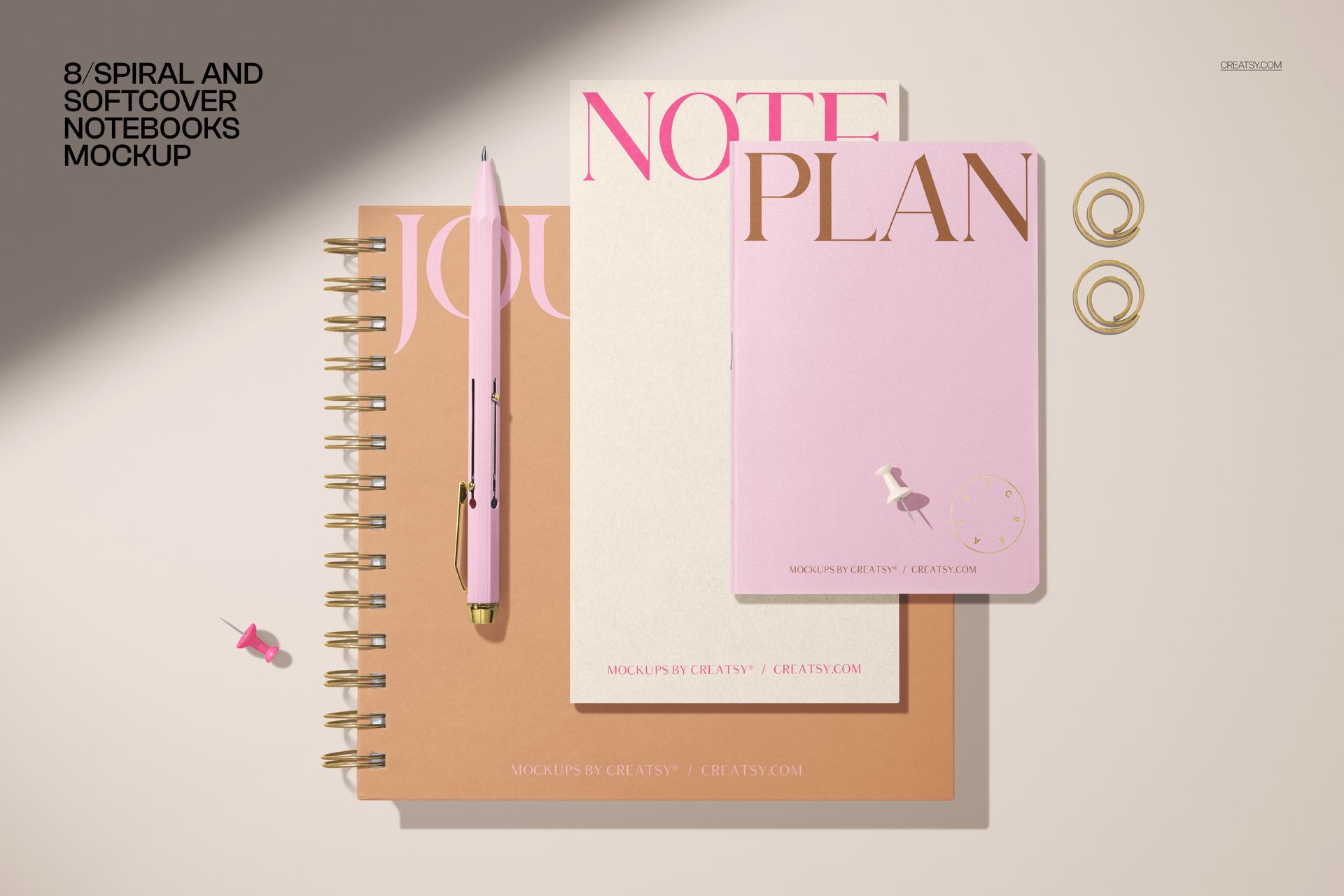 Stationery mockup showing three notebooks with different covers, a pink pen, and gold paper clips on a light surface.