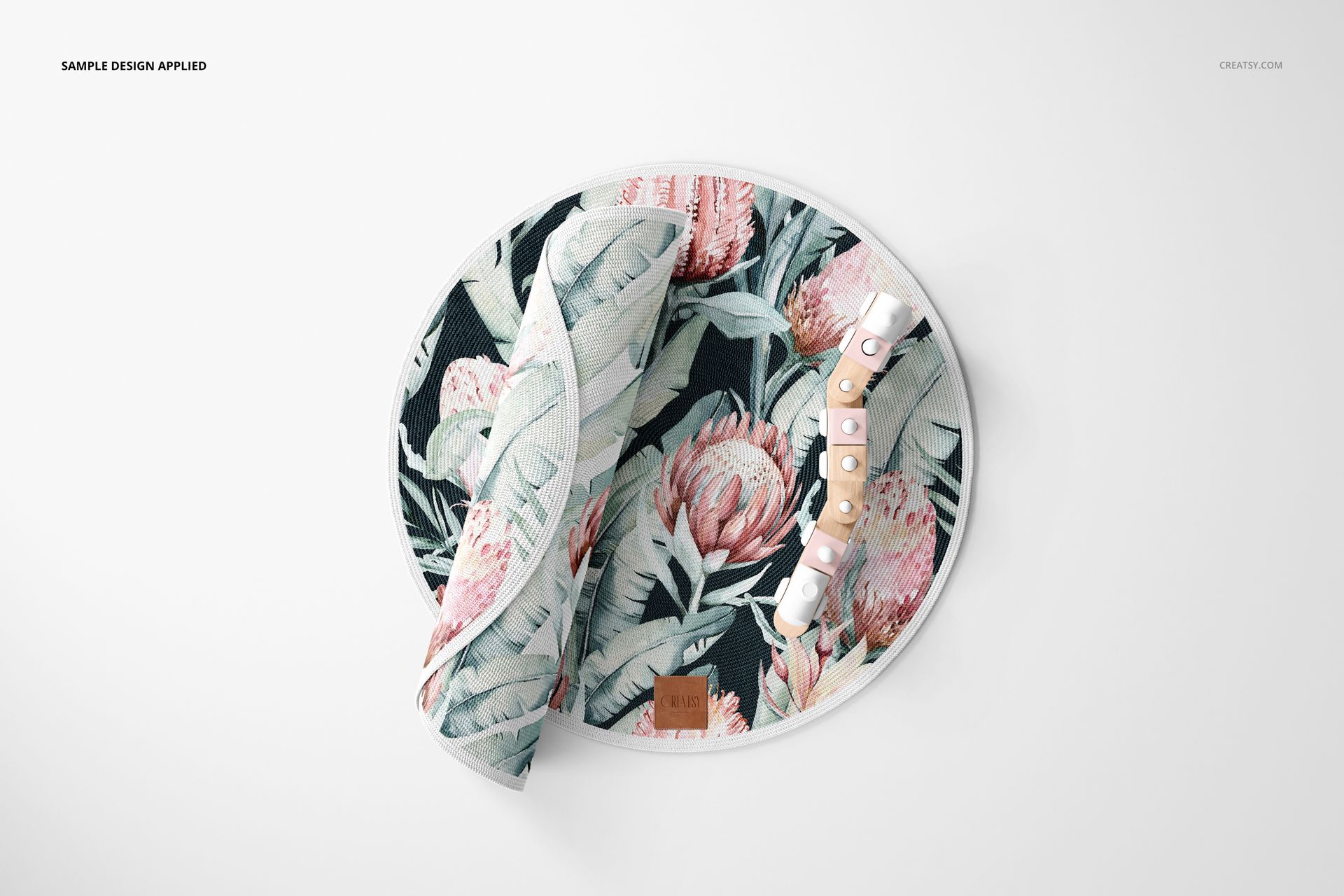 Knitted round rug mockup featuring a tropical floral design, displayed flat with rolled edges and decorative props.