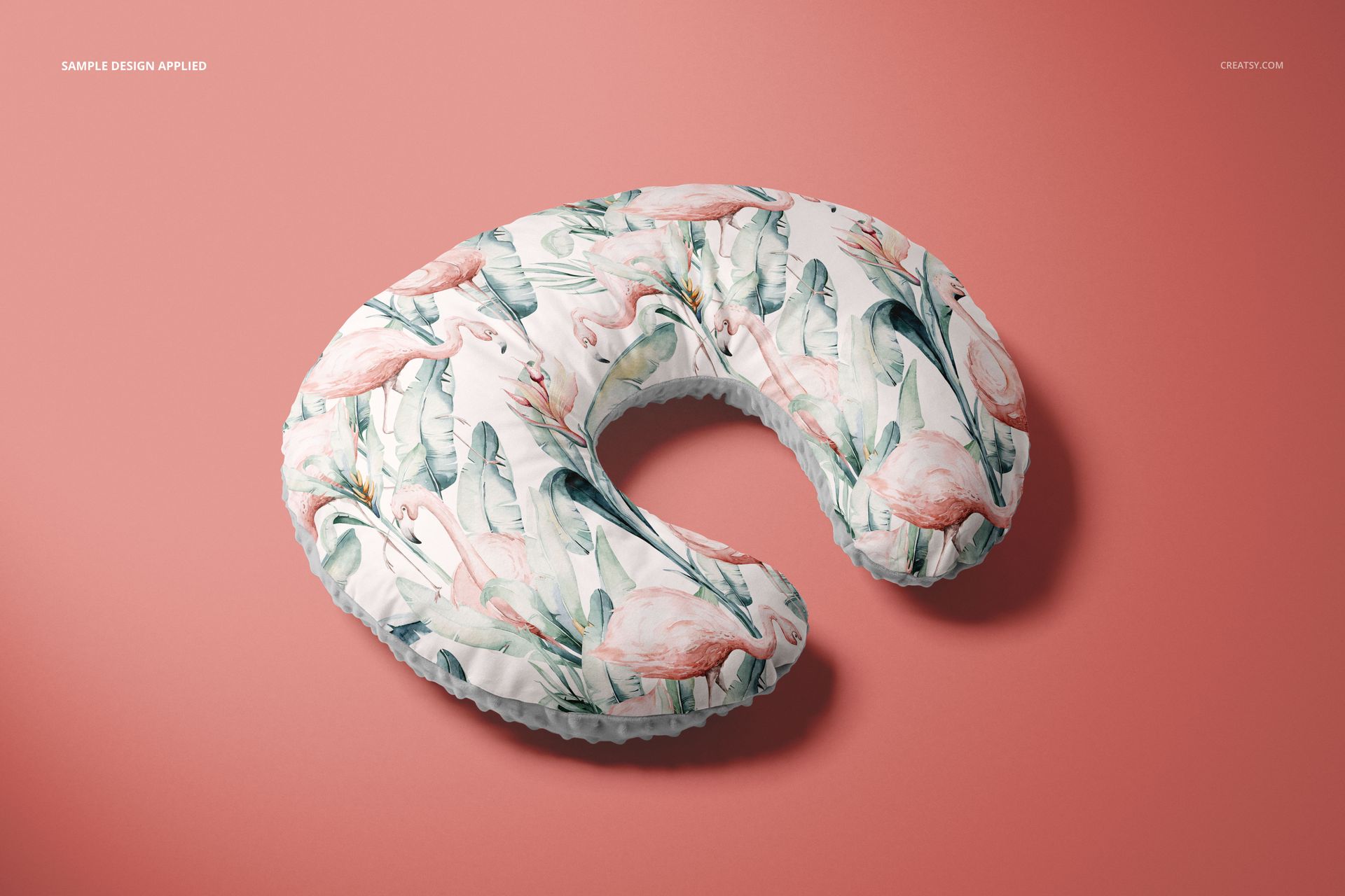Mockup of a nursing pillow cover featuring pastel flamingos and leaves, shown from above on a pink surface.