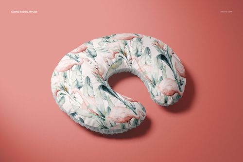 Mockup of a nursing pillow cover featuring pastel flamingos and leaves, shown from above on a pink surface.