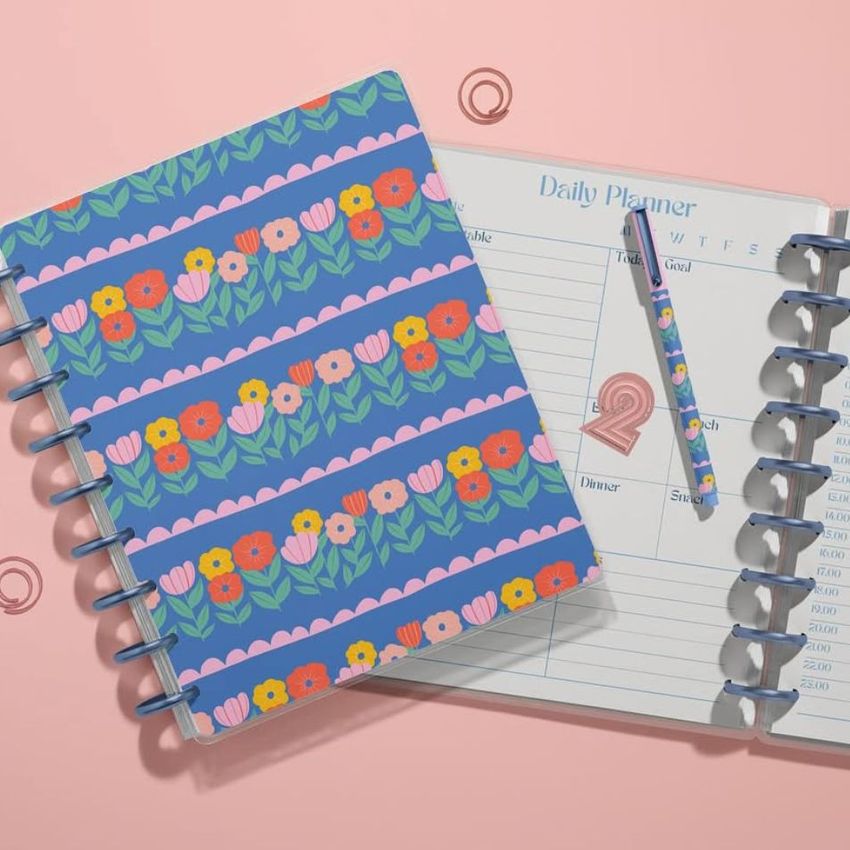 Stationery mockup showing a closed floral planner and an open planner with a daily schedule layout, all on a pastel pink background.