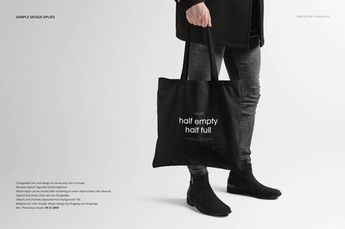 Black tote bag mockup held by a person in dark clothing and boots, displayed from a side perspective.