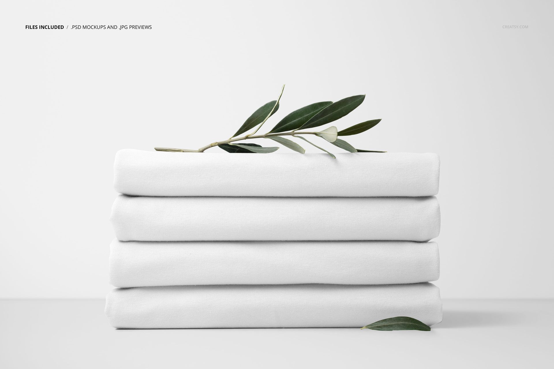 Four neatly folded white jersey fabrics stacked together, accented by green olive branches, presented in a mockup scene.
