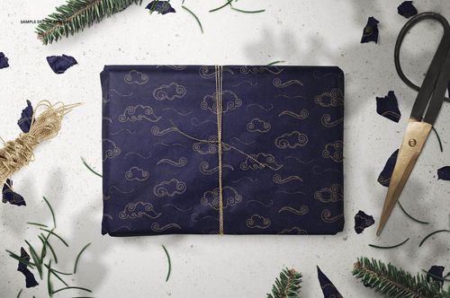 Top view of a wrapped present in navy tissue paper with gold decorative pattern, mockup scene with festive props.
