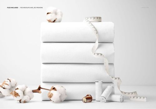PSD mockup showing a pile of white cotton fabrics alongside sewing props like cotton branches, thread spools, and measuring tape.