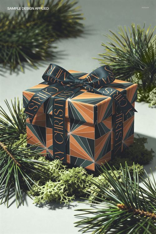 Front view of a square gift box mockup with a bow, featuring bold geometric design and conifers as props.