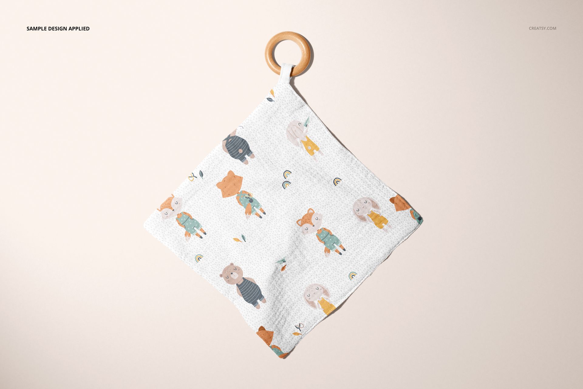 PSD mockup of a square muslin swaddle with wooden teether, showing whimsical animal designs against a neutral background.