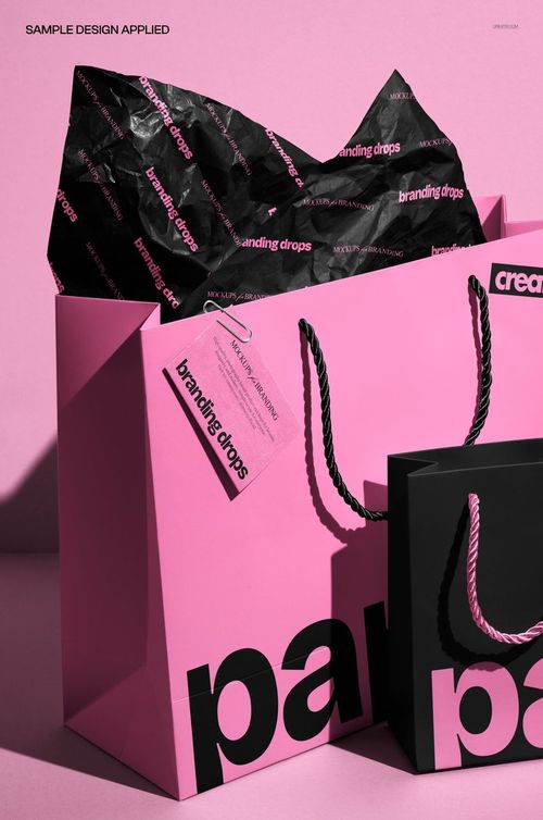PSD mockup showing pink and black paper gift bags with branded tissue paper and attached tag on a pink background.