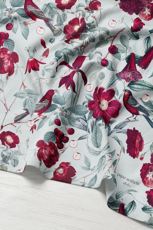 Jersey fabric mockup laid out with gentle folds, featuring a red floral and bird pattern on a pale background.